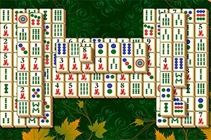 Et brett med mahjong-brikker organisert i et mønster, satt mot en grønn bakgrunn med dekorative detaljer og høstblader