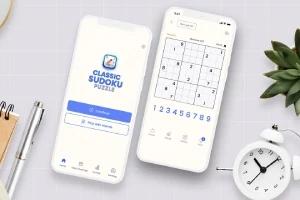 To smarttelefoner som viser en sudoku-app, plassert på et bord ved siden av en plante, en klokke og skrivesaker