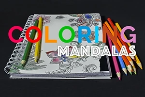 Fargeblyanter og et fargeleggingshefte med mandala-design på en svart bakgrunn