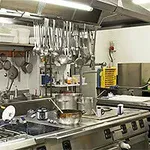 Et travelt restaurantkjøkken med gryter, panner, redskaper og matlagingstilbehør arrangert over komfyrer og hyller
