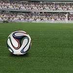 Fotball på gressbane med tribuner i bakgrunnen
