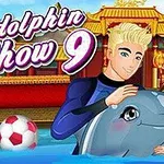 En mann kledd i våtdrakt holder en delfin ved siden av en kvinne, med et ballbasseng og tradisjonelt designet bygning i bakgrunnen