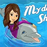 En tegnet jente med en rosa drakt sitter på en delfin i blåttonet vann med teksten My Dolphin Show og en strandball ved siden av