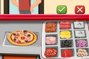 En pizzabenk med ulike ingredienser og en pizza klar til servering, med en person i bakgrunnen