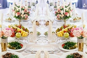 Elegant oppdekking med blomsterarrangementer, fruktfat og dekorative servietter på et langbord