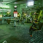 En bar med flere menneskelignende roboter som sitter ved bordene, omgitt av et neonskilt som lyder LE ROBOBAR