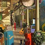 En jernbanestasjon med en blå og gul togvogn, omgitt av kofferter, blomster, en gitar, og to personer som står i nærheten