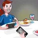 To personer sitter ved et bord med talerken med mat og drikker vin, der den ene holder en spillkonsoll og den andre en telefon